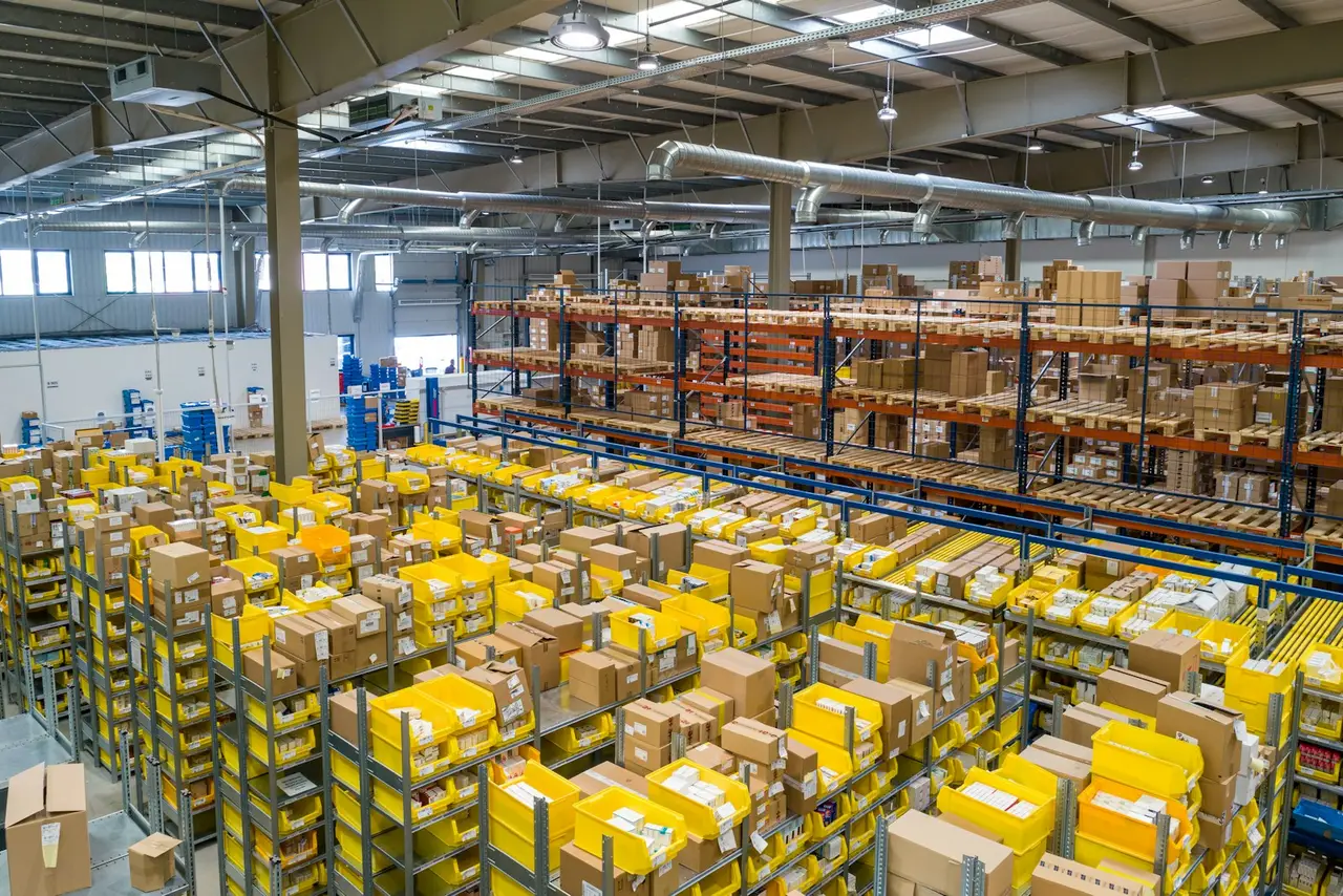 A warehouse aisle with racking full of cardboard cartons and yellow picking bins.